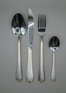 Asgari paslanmaz çelik çatal bıçak seti, tarafsız gri arka planda dikey olarak düzenlenmiş. Gıda blogları, menüler, mutfak tasarımı ve editoryal kullanım için uygun temiz masa ayarlama kavramı.