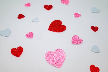 Parlak kalp şekilleri beyaz arka plana saçılmış. Aşk temalı tasarımlar, tebrik kartları, davetiyeler, sosyal medya ve fotokopi alanı olan şenlikli arka planlar için uygun kırmızı, pembe ve beyaz kalpli romantik sevgililer günü konsepti..