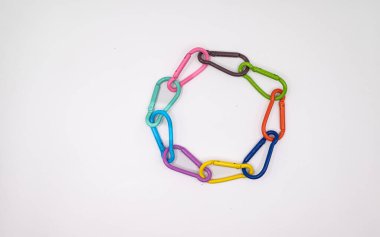 Beyaz arka planda dairesel zincir şeklinde bağlanmış renkli metal karabinalar. Birlik, takım çalışması, çeşitlilik ve güçlü bağın sembolü olarak düzenlenmiş çok renkli parlak klipler. Kopya alanı olan en küçük stüdyo kompozisyonu.