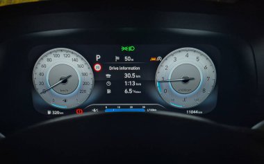 Geceleri ışıklandırılmış hız göstergesi ve takometresi olan modern dijital araba paneli. Sürücü bilgisini, yakıt tüketimini, sıcaklığı ve uyarı göstergelerini gösteren araç kümesi görüntüsü.