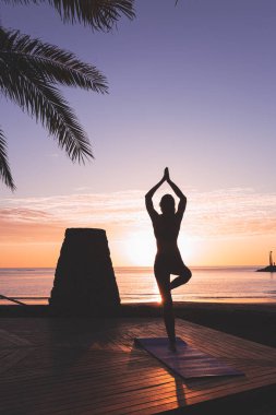 Genç bir kadının silueti gün doğumunda plajın önünde meditasyon yapıyor..