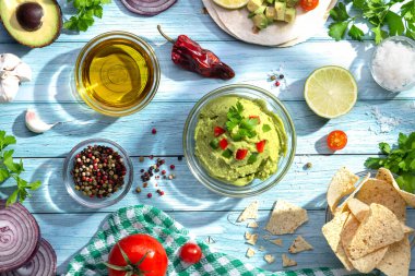 Bir kase guacamole ve mavi arka planda malzemeler. Üst görünüm.