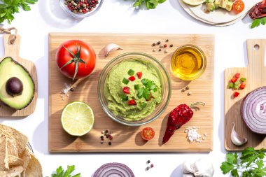 Düz kompozisyon. Tahta tahtada beyaz arka planda malzemeleri olan guacamole..