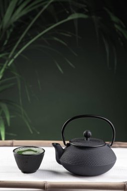 Yeşil arka planda beyaz ahşap zeminde kibrit çayı ve çaydanlık. Geleneksel Japon içkisi. Dikey biçim.