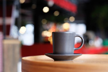 Küçük siyah bir kahve fincanı ahşap bir masada bir fincan üzerinde. Arka planda bulanık arka planda bir kafede kahve.