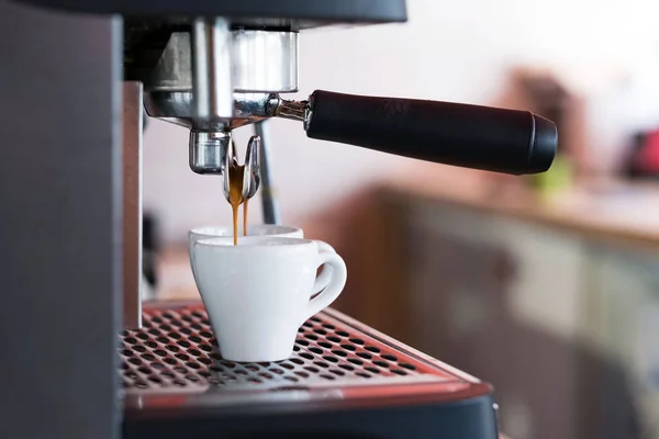 The espresso machine pours two coffees into white cups.