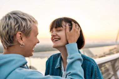 Genç, şehvetli lezbiyen çiftin gülüşünü yakın çekim. Gün doğumunda köprüde yan yana dururken romantik anların tadını çıkarıyorlar.