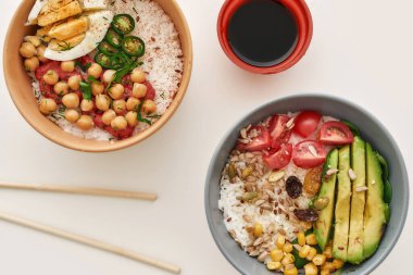Dilimlenmiş sebze, pilav, yemek çubuğu ve soya sosuyla beyaz arka planda izole edilmiş iki kasenin üst görüntüsü.