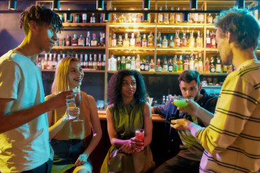 Çekici genç kadınlar bar tezgahında kokteyl içip yeni tanıştıkları erkeklerle sohbet ediyorlar. Genç yetişkinler gece kulübünde flört ederken içki içiyorlar.