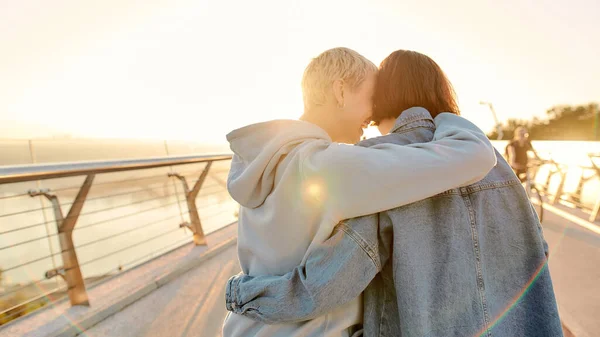 Casal lésbico em pé na ponte, abraçando um ao outro enquanto admirava o nascer do sol juntos. Homossexualidade, LGBT e conceito de amor — Fotografia de Stock