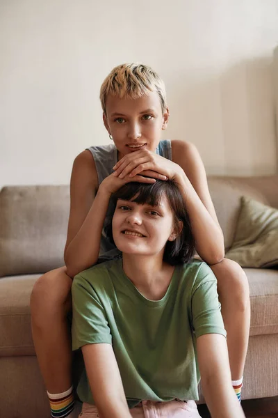 Porträtt av unga kvinnor som ser glada ut medan de myser och kopplar av hemma. Lesbiska par tillbringar tid tillsammans inomhus — Stockfoto