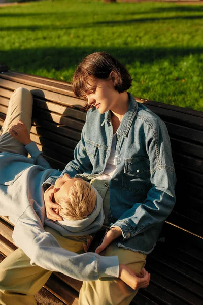 Dos mujeres jóvenes relajándose en el banco en el parque de la ciudad en un día soleado. Lesbianas pareja pasando tiempo juntos al aire libre — Foto de Stock