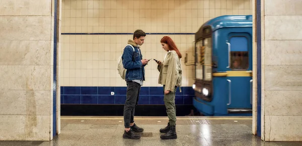 Полнометражный снимок пары подростков, использующих смартфоны, полностью поглощенных онлайн жизнью, игнорирующих друг друга, стоя на станции метро — стоковое фото