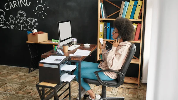 Active african american woman calling from charitable organization office, Young volunteer working for a charity, donating apparel to needy people