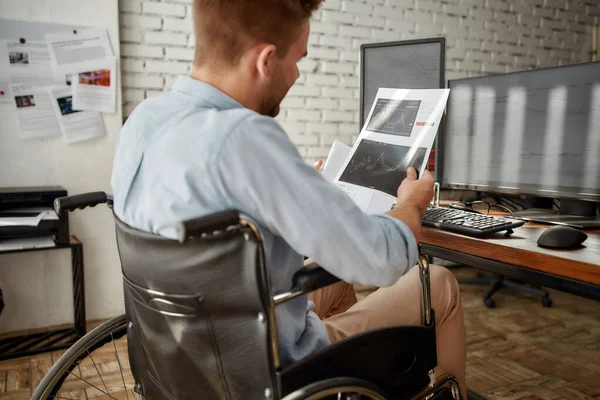 Analizlerle çalışıyorum. Tekerlekli sandalyedeki genç, profesyonel erkek tüccarın modern ofisindeki iş yerinde çalışırken hisse senedi grafiği raporunu analiz etmesi. — Stok fotoğraf