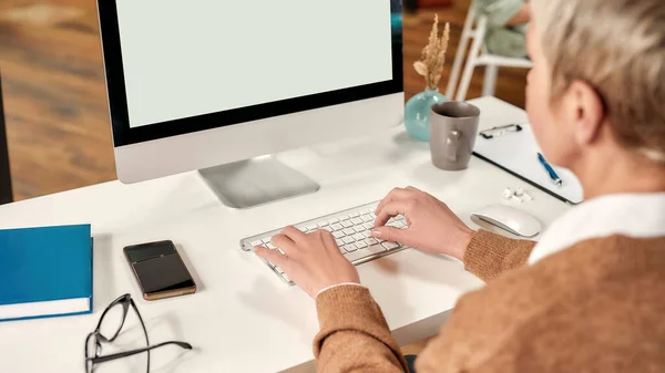 Une femme mûre blanche bien habillée avec une coupe de cheveux courte assise à une table travaillant sur son PC — Photo