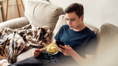 Genç adam evdeki kanepede otururken cep telefonu kullanıyor. Akıllı telefon bağımlılığı kavramı