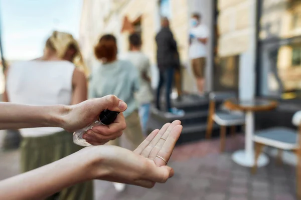 Primer plano de las manos de la mujer usando desinfectante de manos, limpiando las manos con spray desinfectante de alcohol mientras está de pie en la fila para recoger su pedido durante el bloqueo del coronavirus — Foto de Stock