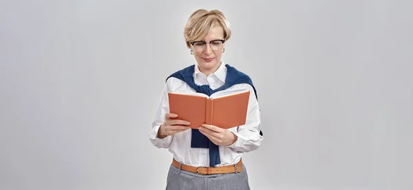 Portrait d'une élégante femme caucasienne d'âge moyen portant des vêtements d'affaires et des lunettes, regardant son carnet tout en restant isolée sur fond gris — Photo