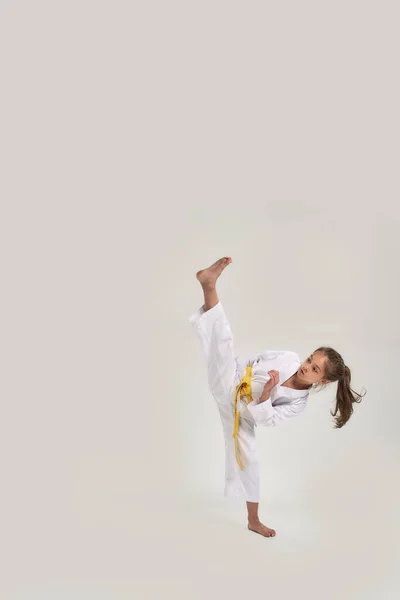 Tiro de comprimento total de menina karatê em quimono branco com uma faixa amarela exercitando e lutando, fazendo artes marciais, de pé isolado sobre fundo branco — Fotografia de Stock