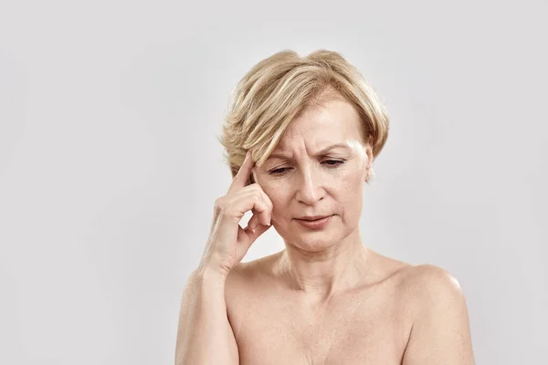 Portrait of beautiful blonde middle aged woman with puzzled expression, thinking deeply about something, posing isolated against grey background. Body language and face expression concept — Stock Photo, Image