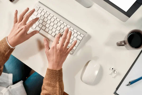 Un primo piano di una donna matura bianca mani digitando su una tastiera seduta a un tavolo di fronte a un PC — Foto Stock
