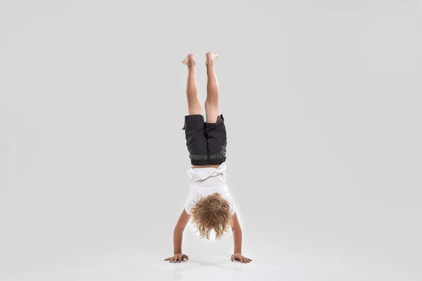 Full length shot of little playful boy child standing on his arms with legs pointing upwards isolated over grey background — Stock Photo, Image