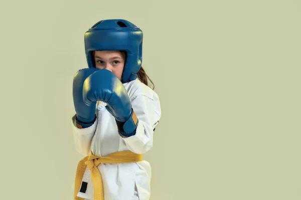 Retrato de menina karatê em quimono branco usando luvas e capacete de proteção, olhando focado na câmera, pronto para socar, fazendo artes marciais isoladas sobre fundo verde — Fotografia de Stock