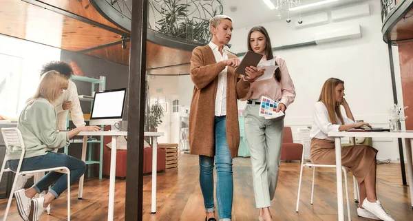 Dos mujeres bien vestidas caminando juntas a través de una oficina moderna hablando entre sí —  Fotos de Stock