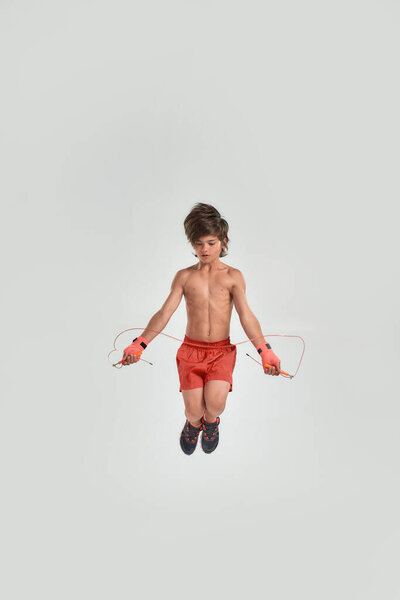 Маленький спортивный мальчик боксер с боксерской повязкой на руках, с помощью скакалки, прыжки изолированы на белом фоне