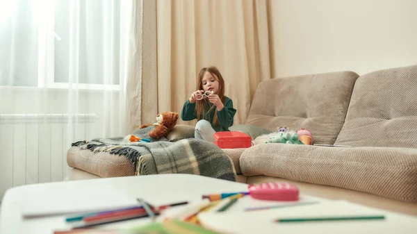 Uma menina littile que joga com um brinquedo que senta-se em um sofá que tem seus brinquedos ao redor em um quarto brilhante grande — Fotografia de Stock