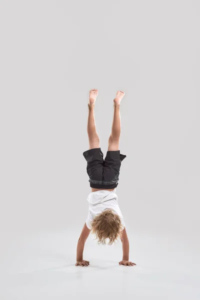 Tiro de comprimento total de criança menino brincalhão de pé em seus braços com as pernas apontando para cima isolado sobre fundo cinza — Fotografia de Stock