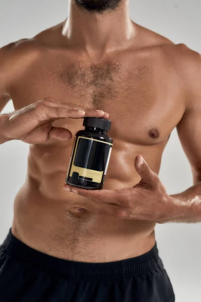 Muscular athlete holding bottle of sport vitamins — Stock Photo, Image