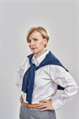 Gri arka planda soyutlanmış bir şekilde poz verirken iş elbisesi giymiş zarif orta yaşlı beyaz kadın portresi.