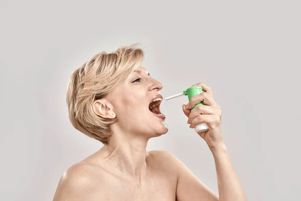 Retrato de mulher de meia-idade atraente usando spray de garganta, de pé isolado sobre fundo cinza — Fotografia de Stock