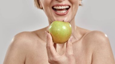 Elinde yeşil elmayla gülümseyen orta yaşlı kadının elini kapat. Gri arka planda izole bir şekilde poz ver.