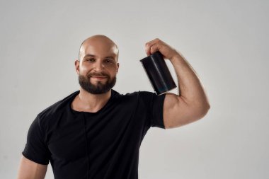 Gülümseyen Kafkasyalı genç vücut geliştirici pazıların üzerinde spor besin şişesi tutuyor.