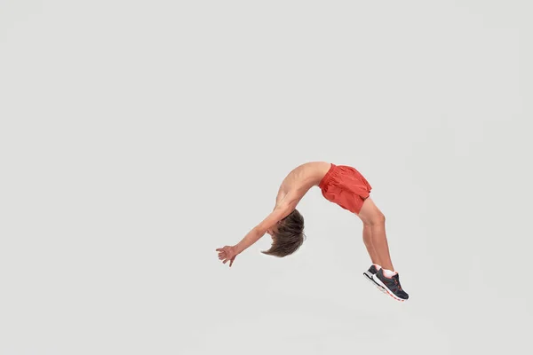 Volledige shot van kleine sportieve jongen kind in shorts springen, tonen flexibiliteit geïsoleerd over witte achtergrond — Stockfoto
