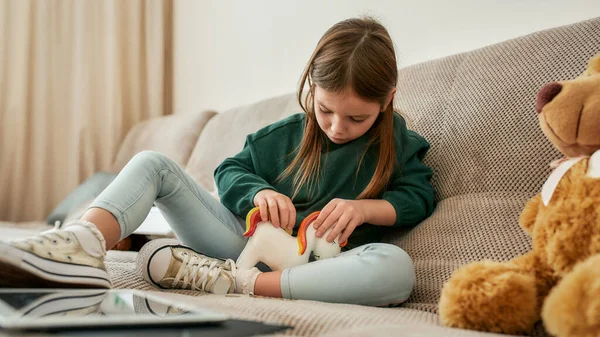 Una niña está llenando su lujosa caja de dinero unicornio con un montón de monedas, su oso de peluche está sentado a su lado — Foto de Stock