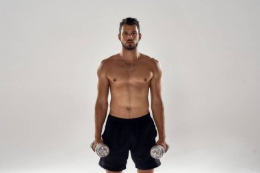 Genç yakışıklı kaslı beyaz adam dambılları kaldırıyor.