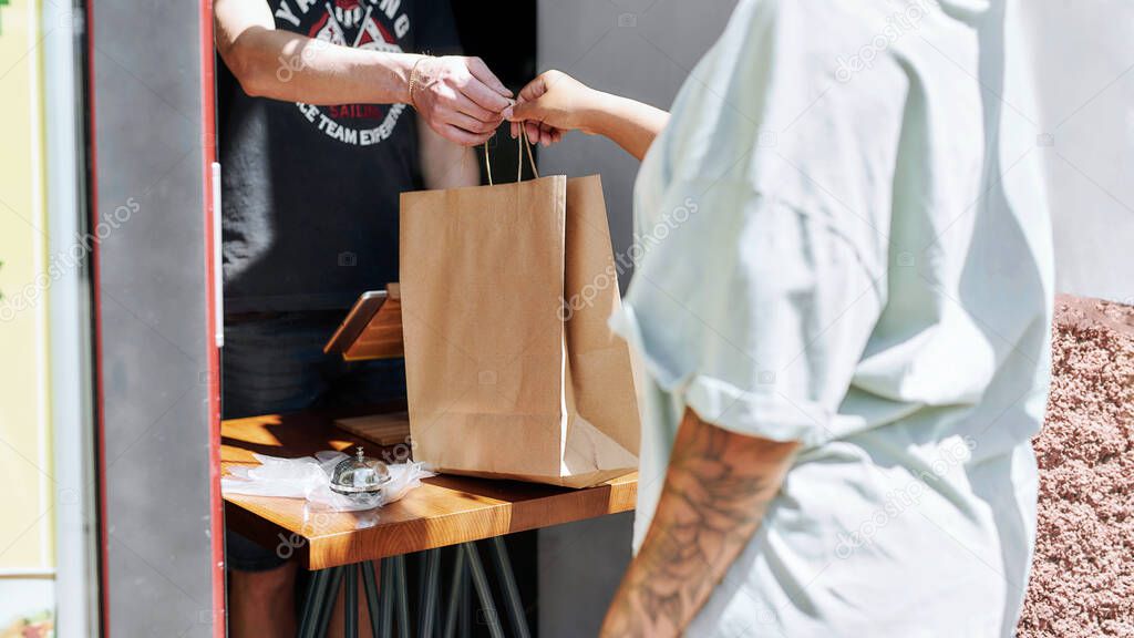 Cropped shot of woman taking paper bag with her order from hands of shop assistant while collecting her purchase from the pickup point