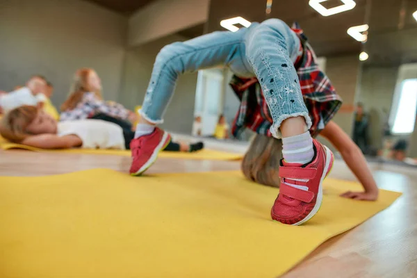 Παραμονή ευέλικτη. Κοριτσάκι κάνει ανάποδη στροφή στο στρώμα γιόγκα στο στούντιο χορού. Ομάδα παιδιών που κάνουν γυμναστικές ασκήσεις — Φωτογραφία Αρχείου