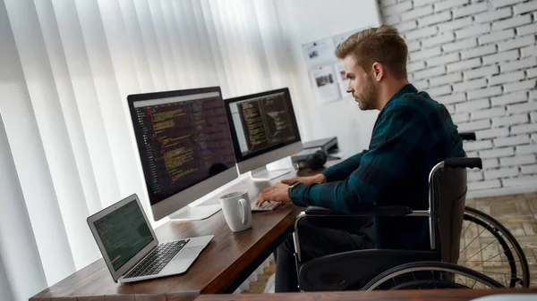 Bilgisayar programı yazılıyor. Modern ofisteki iş yerinde otururken tekerlekli sandalyede çalışan genç bir web geliştiricisinin çoklu bilgisayar ekranında program kodunun yan görüntüsü. — Stok fotoğraf