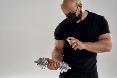 Kafkasyalı genç bir adam dambıl üzerine antiseptik püskürtüyor.