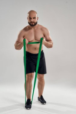 Genç kaslı erkek atlet lastik bant çekiyor.