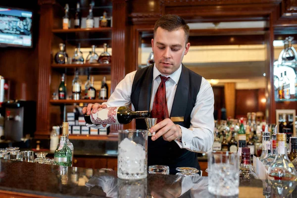 Os empregados de bar fazem melhor. Jovem barman de pé no balcão e derramando vinho tinto para preparar coquetel gelado no bar — Fotografia de Stock