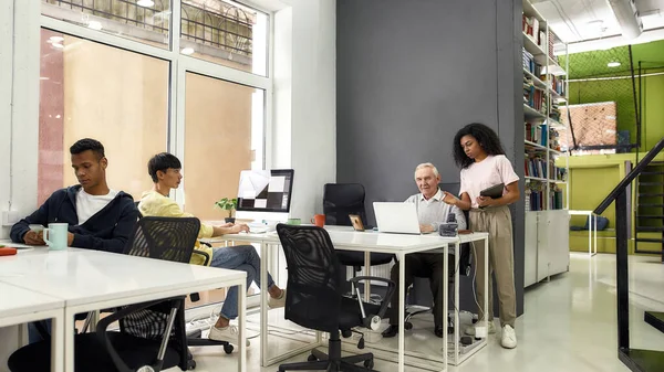 Full length shot of aged man, senior intern listening to his young colleague, Friendly female worker training or teaching new employee, preparing for first day at work — Stock Photo, Image