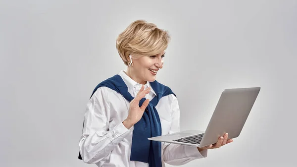 Ritratto di elegante donna caucasica di mezza età che indossa abiti da lavoro con laptop in mano, mentre ha una videochiamata online, isolata su sfondo grigio — Foto Stock