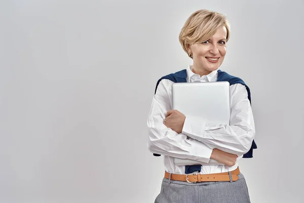 Retrato de una elegante mujer caucásica de mediana edad que lleva un atuendo de negocios sosteniendo la computadora portátil, sonriendo a la cámara mientras posa aislada sobre un fondo gris —  Fotos de Stock