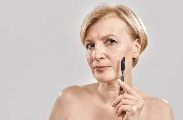 Portrait of attractive middle aged woman looking at camera while holding medical scalpel in her hands isolated over grey background — Stock Photo, Image